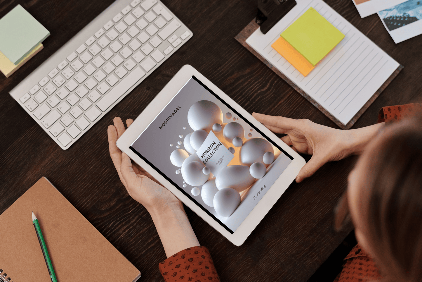 Person using a tablet on a desk with a keyboard and stationery items.