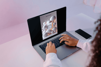 Person using a laptop with a screen displaying a product image on a light pink background