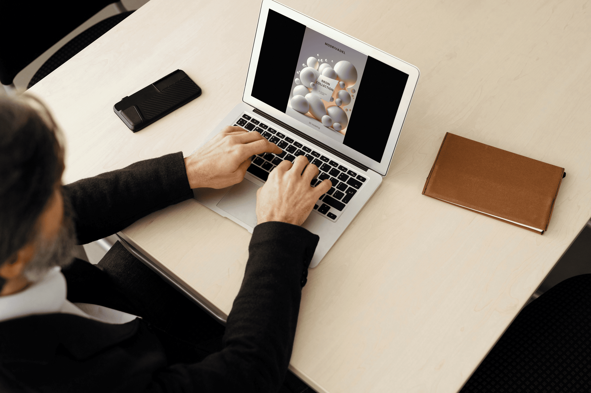 Person using a laptop on a desk with a phone and notebook nearby