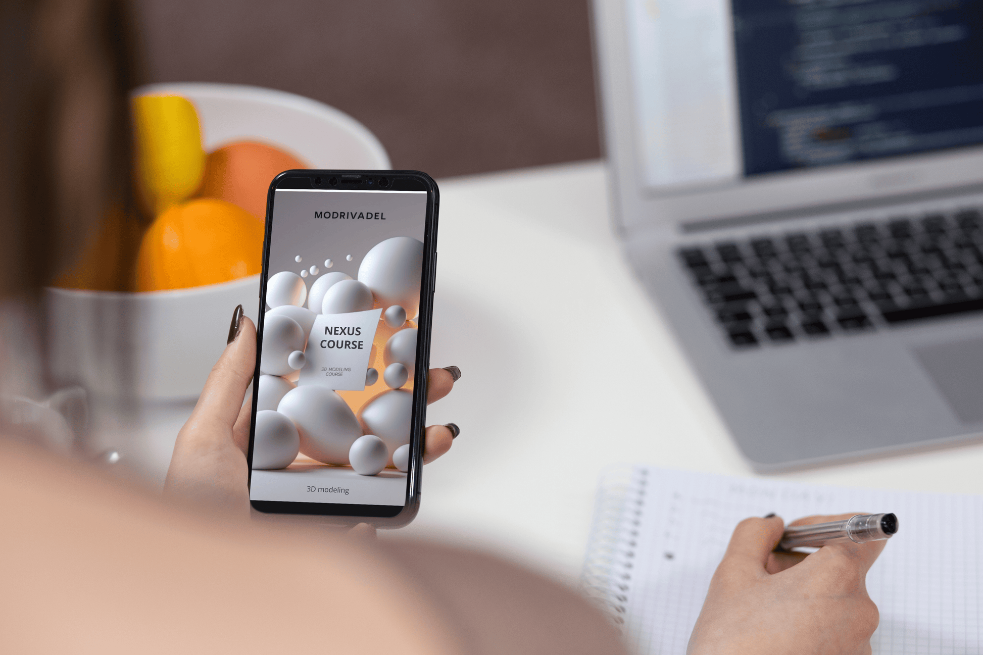 Person holding a smartphone with a product display, sitting at a desk with a laptop and bowl of fruit.