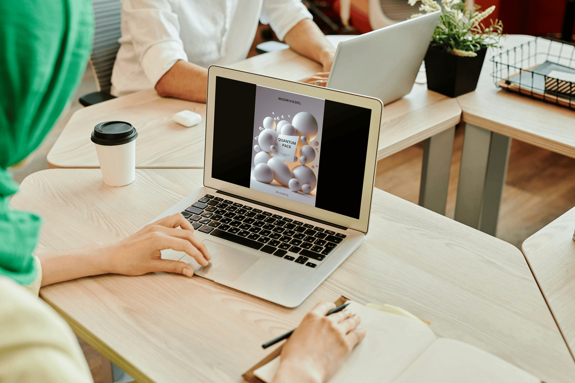 Person using a laptop with a colleague in the background at a desk.
