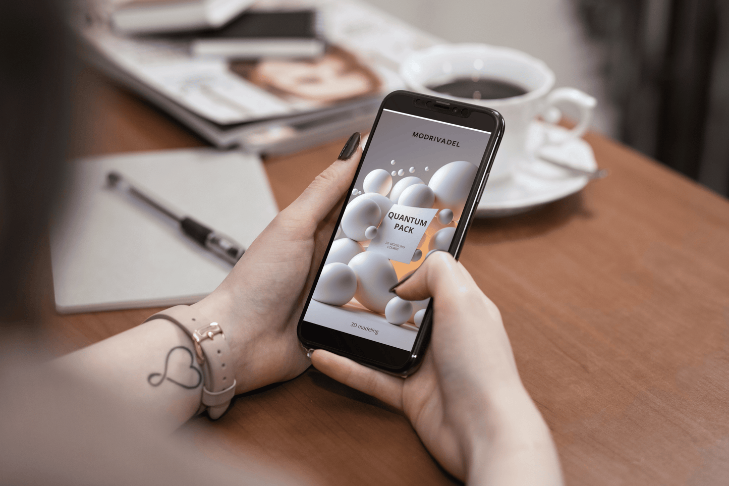 Person holding a smartphone with an 3D modelling course on a table with a notebook and coffee cup.